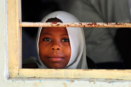 A schoolgirl watches from her classroom as members of the 414th Civil Affairs Battalion, Civil Affairs Team Four, unload books to be given to a local primary school in Tanga, Tanzania. More than 1,000 donated books were given to local schools during the book drop.